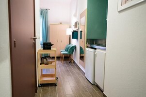 Um corredor estreito com cozinha compacta, uma pequena mesa com cadeiras e um carrinho com utensílios de cozinha.