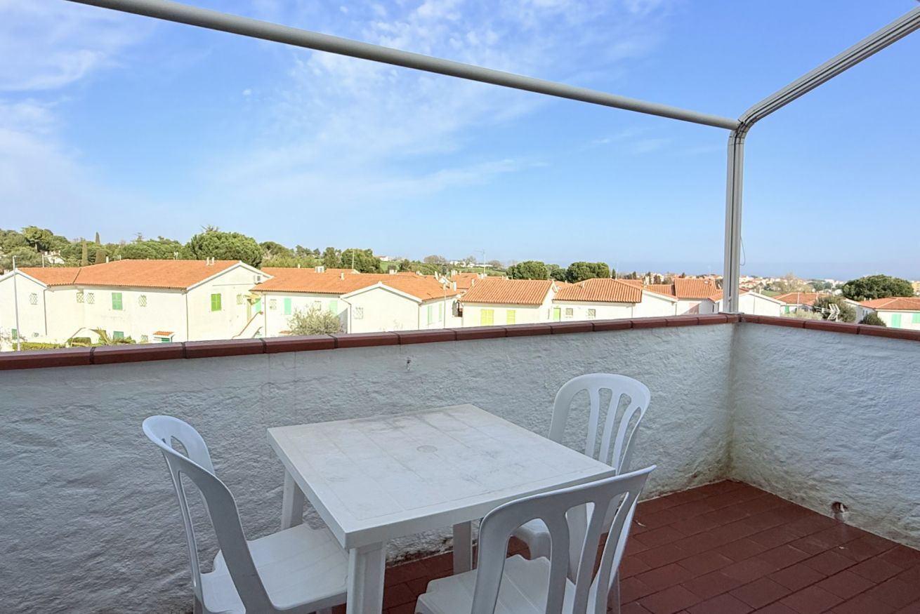 Un balcón con una mesa y sillas blancas, con vistas a una zona residencial de tejados rojos.
