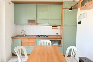 Una cucina compatta con mobili verdi, un tavolo di legno e sedie bianche.