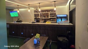 Un espace bar avec un comptoir, des étagères remplies de bouteilles d’alcool, un téléviseur et une table ornée d’un vase de tournesols.