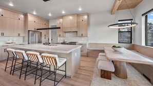 A modern kitchen with wooden cabinets, a central island with bar stools, a dining table with benches, and a hanging light fixture. - Dual-Homes, 10br10ba, Sleeps 32, 2 HotTubs-Views (Heber City)