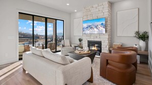 A modern living room with a fireplace, a sofa, a coffee table, and a TV mounted on a stone wall. - Dual-Homes, 10br10ba, Sleeps 32, 2 HotTubs-Views (Heber City)