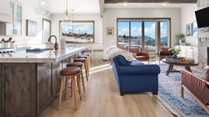 A modern kitchen with a bar area, wooden stools, and a view of a snowy landscape through large windows. - Dual-Homes, 10br10ba, Sleeps 32, 2 HotTubs-Views (Heber City)
