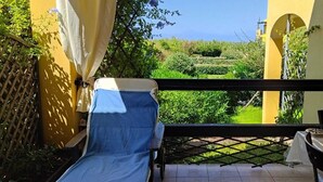 En balkon med en blå stol, et bord og udsigt over en have og en bygning.