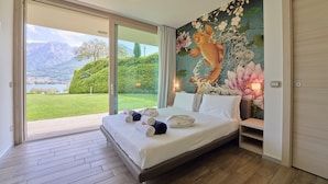 A bedroom with a large bed, a view of a garden, and a mural of a fish and lotus. - Villa Costanza (Oliveto Lario)