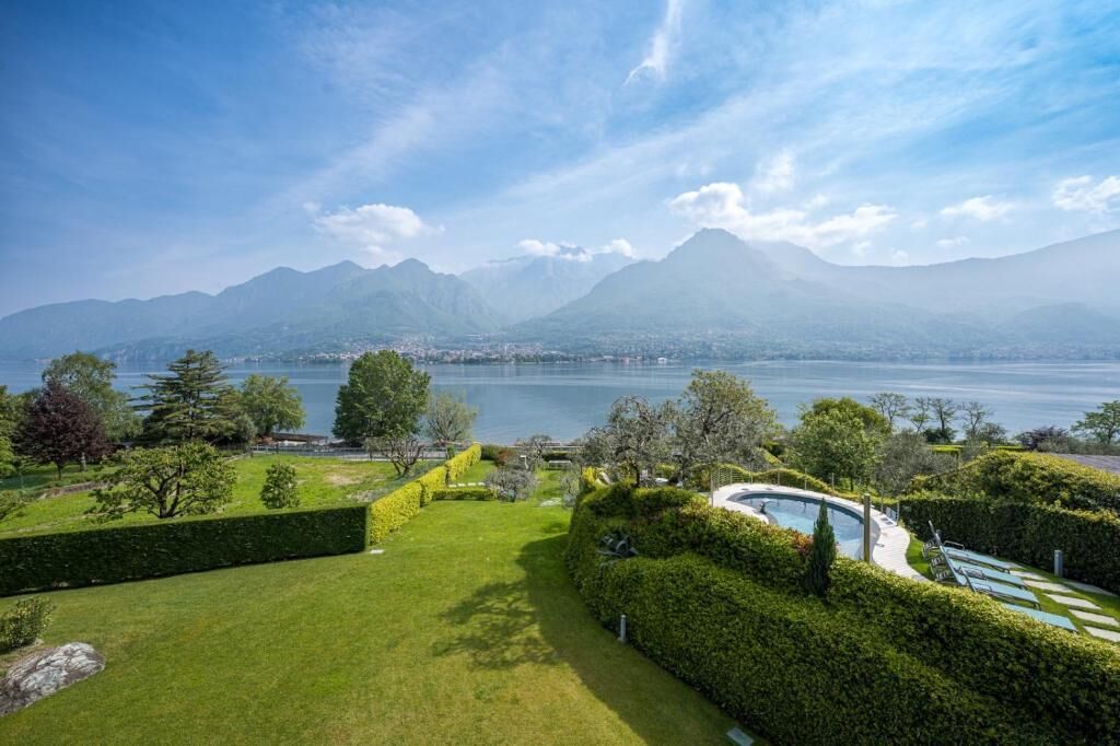 Ein angelegter Garten mit Schwimmbad, Blick auf einen See und Bergen im Hintergrund.