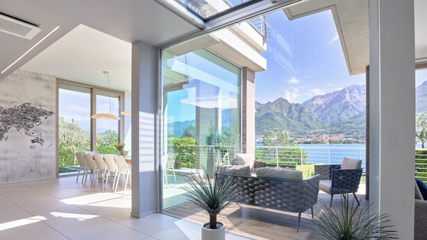 A modern interior with a large glass door leading to a balcony with mountain views. - Villa Costanza (Oliveto Lario)