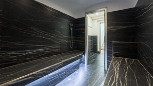 A modern bathroom with black marble walls and floors, a glass shower enclosure, and a bench. - Villa Costanza (Oliveto Lario)