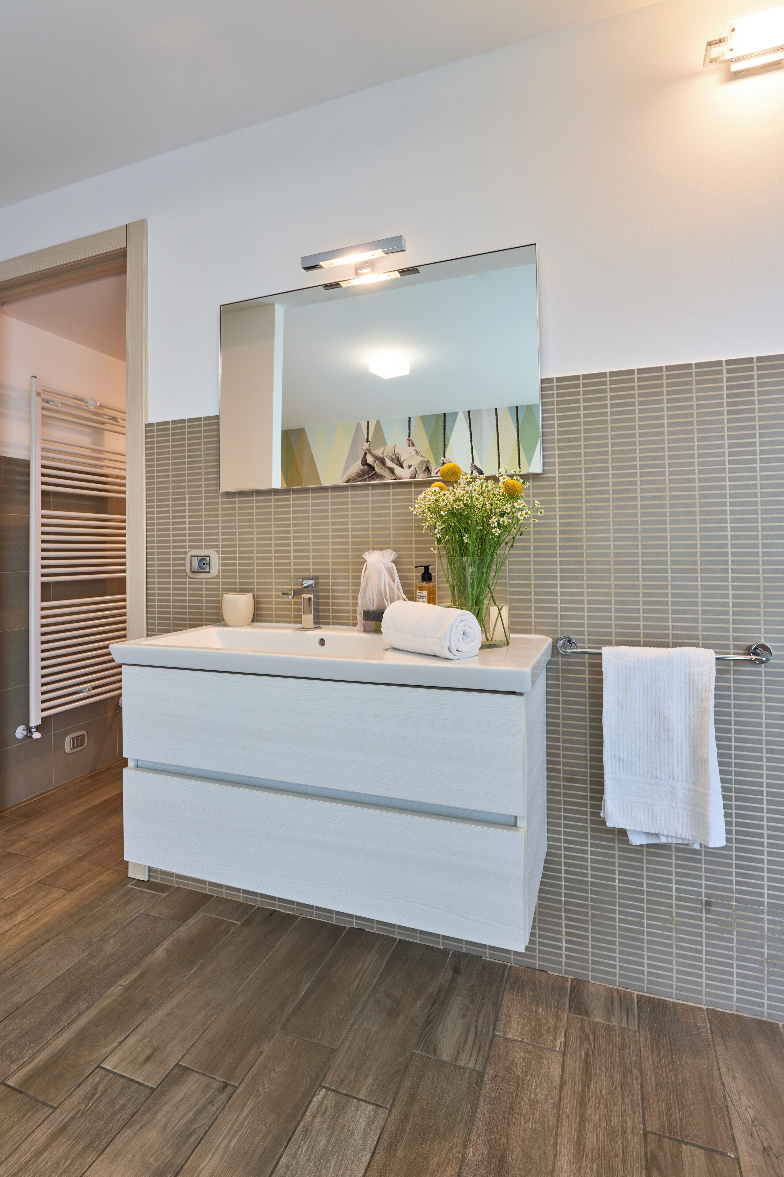 Un baño moderno con un tocador blanco grande, un espejo, un perchero y piso de madera.