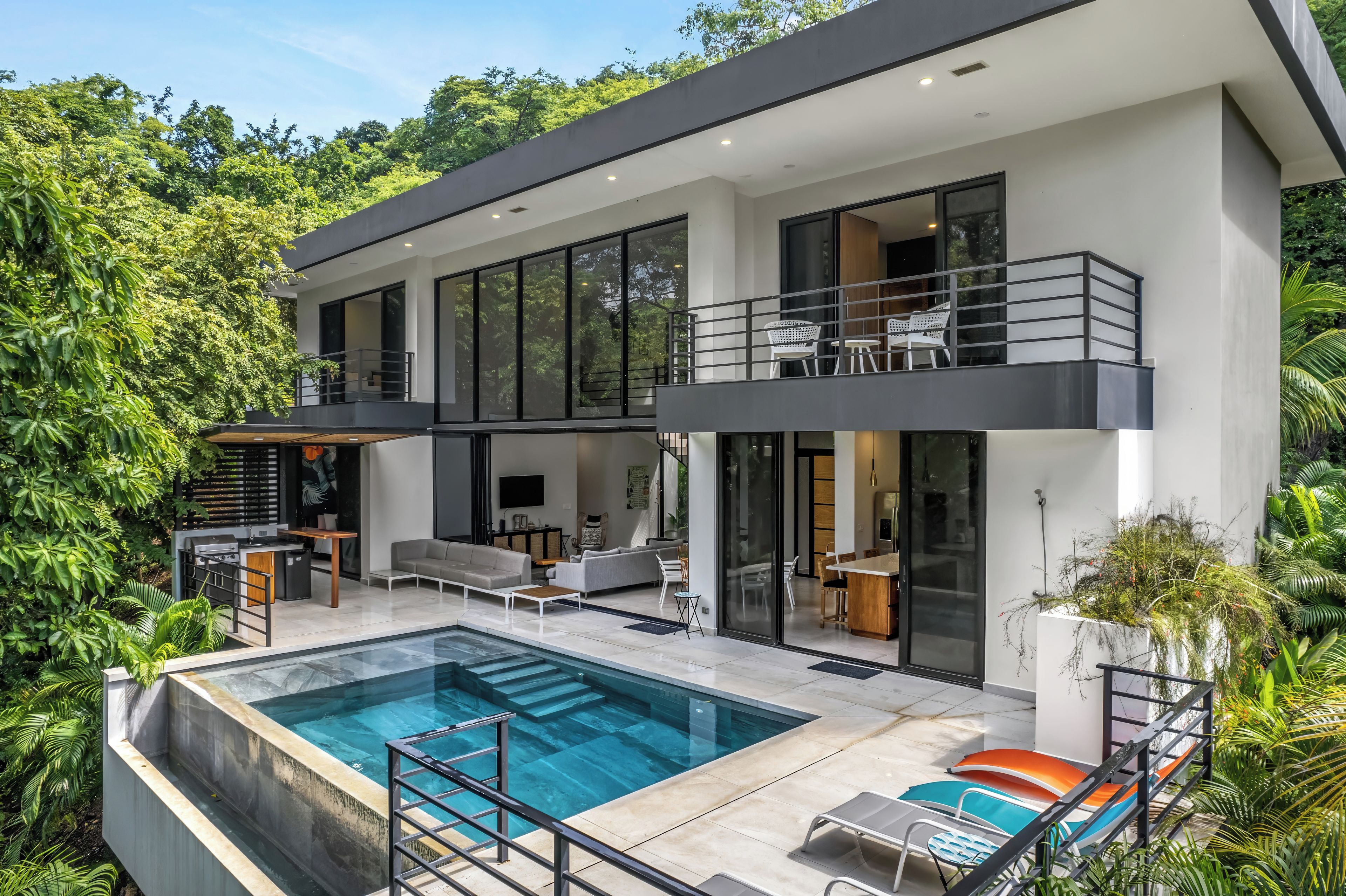 A modern two-story house with a swimming pool, outdoor seating, and a balcony.