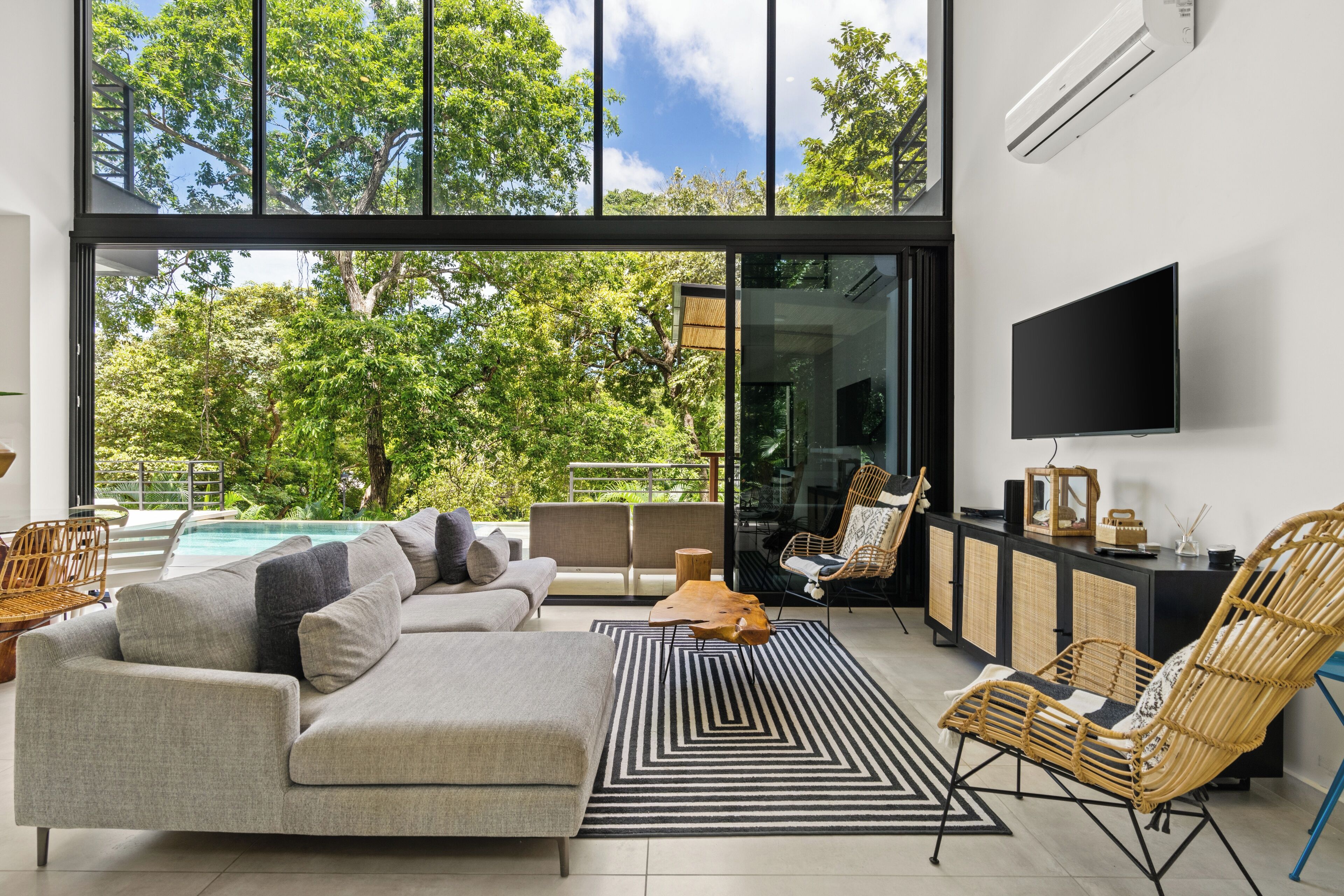 A modern living room with a large window, a sofa, a chair, and a flat-screen TV.
