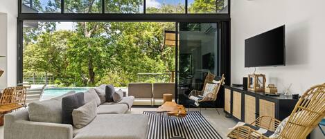 A modern living room with a large window, a sofa, a chair, and a flat-screen TV.