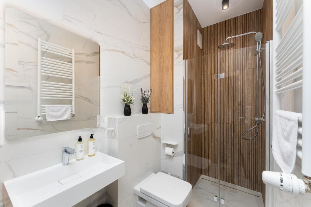 Uma casa de banho moderna com toucador branco, cabine de duche em vidro e painel de parede em madeira.