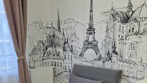 A living room with a grey sofa, a patterned rug, and a wall mural of Parisian architecture.
