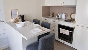 A modern kitchen with white cabinetry, a dining area with grey chairs, and a built-in oven.