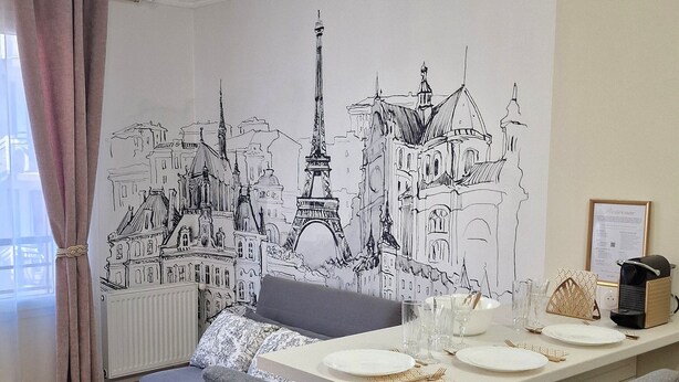 A dining area with a table set for four, a sofa, and a wall mural of Parisian architecture.