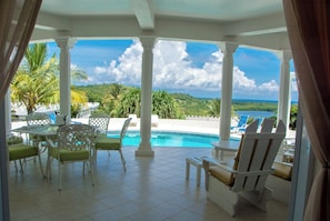 A covered outdoor area with a pool, white columns, and green chairs.