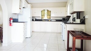 A kitchen with white cabinets, a microwave, a kettle, and a small wooden table with a wire basket. - Castles in Paradise - by Zenbreak (Vieux Fort)