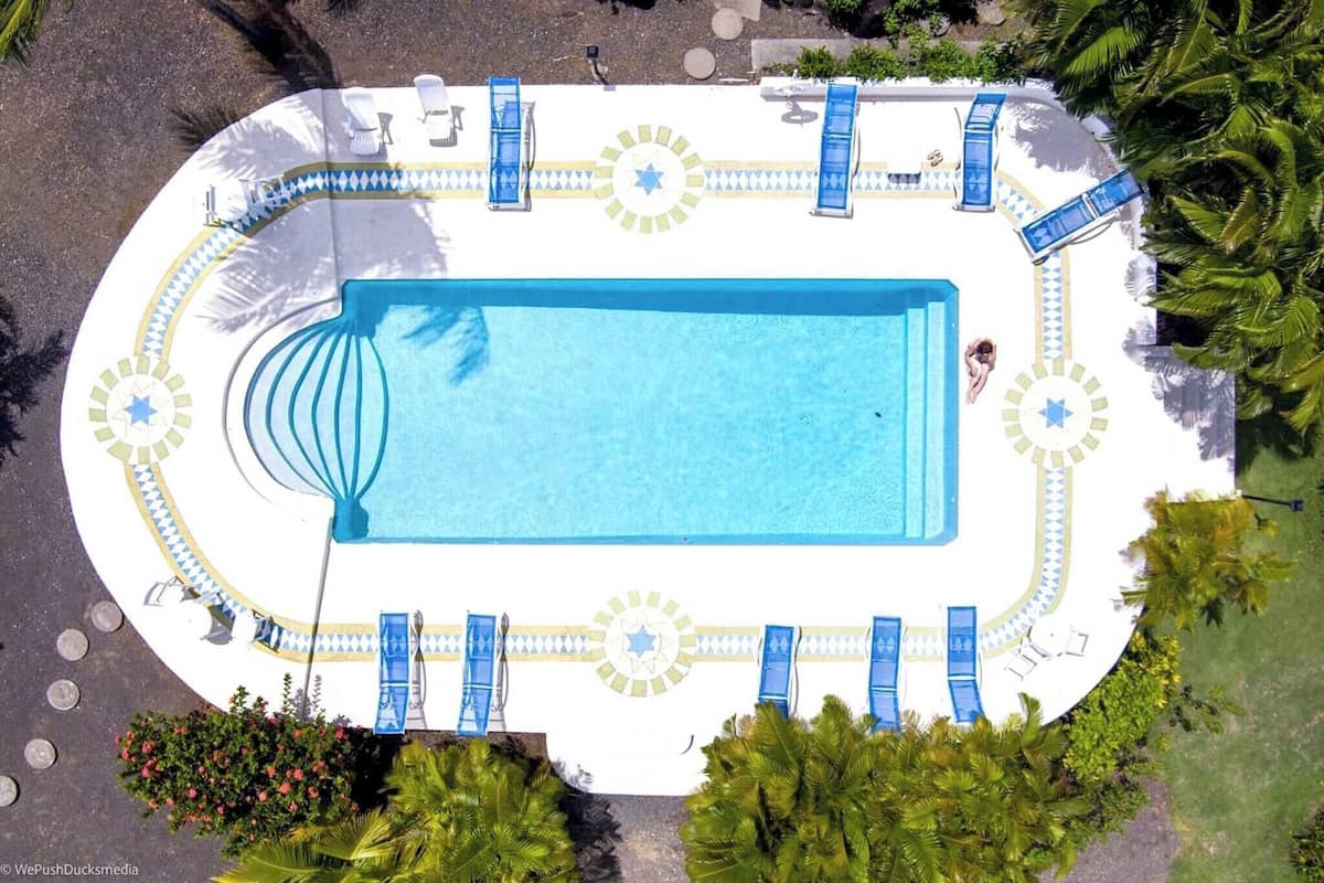 An aerial view of a rectangular swimming pool with blue water, surrounded by white deck with blue lounge chairs and sun loungers.