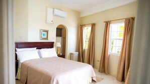 A bedroom with a bed, a nightstand, an air conditioning unit, a window with curtains, and a wall-mounted picture. - Castles in Paradise - by Zenbreak (Vieux Fort)