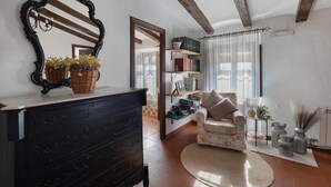 A room with a dark wooden dresser, a floral armchair, a round woven rug, and a bookshelf with books and decorative items.
