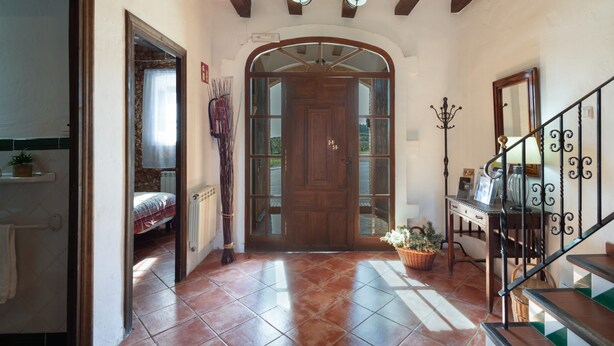 A hallway with a wooden door, a staircase with a wrought iron railing, and a tiled floor.