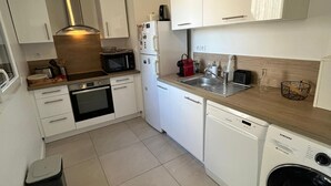 Una cocina compacta con armarios blancos, microondas, refrigerador, lavaplatos, horno y lavavajillas.