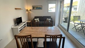 Un comedor con una mesa de madera y cuatro sillas, un sofá, un televisor y un ventanal con vistas al exterior.
