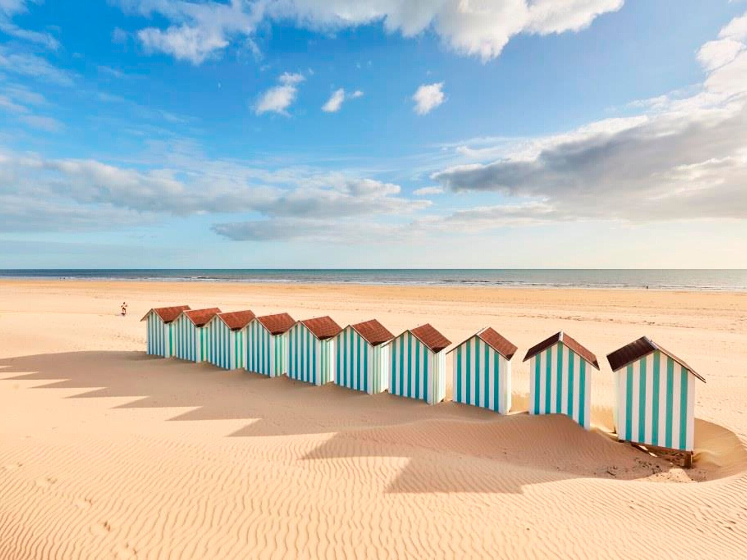 A row of beach huts on a sandy beach with a clear sky.