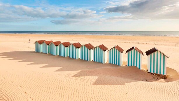 Une rangée de cabanes de plage sur une plage de sable, sous un ciel dégagé.
