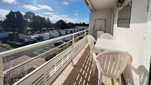 A balcony with a view of a parking lot and buildings, white chairs, and a table. - Appartement lumineux avec terrasse – Arcachon, Ville d’Automne (Arcachon)