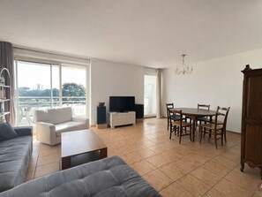 Ein großzügiger Wohnbereich mit Sofa, Couchtisch, Esstisch mit Stühlen, Fernseher und Bücherregal.