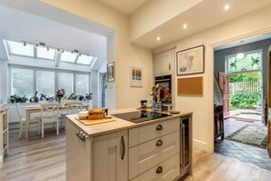 A spacious kitchen with a large island, a dining area with a table and chairs, and a view of a garden through an open door. - Nithen Lodge · Hot Tub + Fire Pit & Dog-Friendly (Buxton)