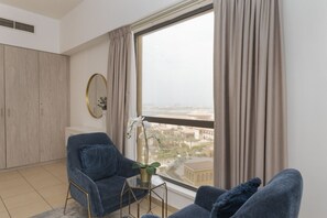 A modern living room with a large window, a sofa, a small table, and a decorative plant. - Cozy JBR 2BR Retreat | Steps to the Beach & The Walk (Dubai)