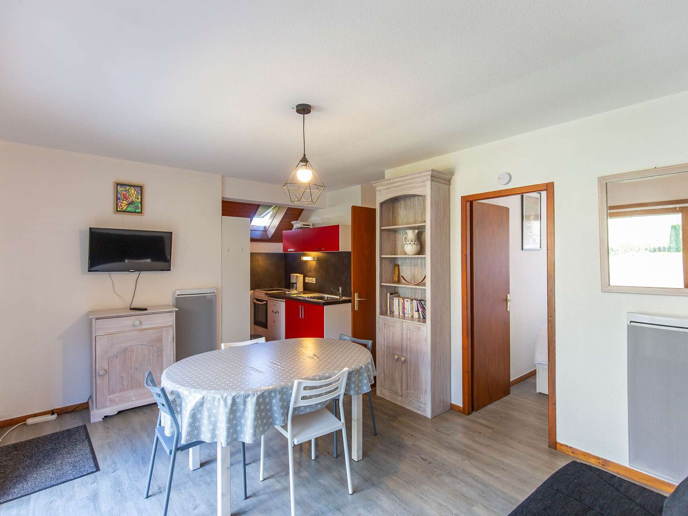 A compact living space with a dining area, kitchenette, and a TV mounted on the wall.