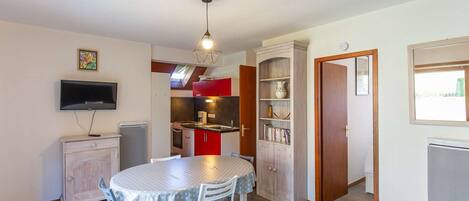 A compact living space with a dining area, kitchenette, and a TV mounted on the wall.