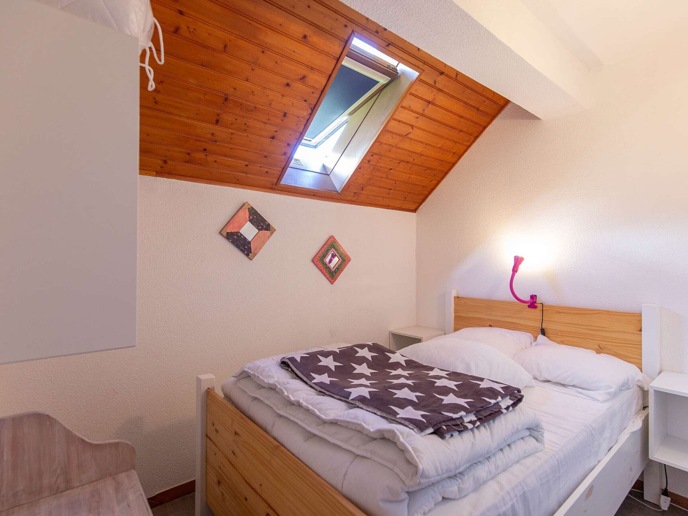 Une chambre avec un plafond en pente, un puits de lumière, un lit recouvert d’une couverture à motifs d’étoiles et deux éléments décoratifs sur les murs.