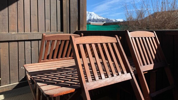 Sillas de madera y una mesa en una terraza con vistas a una montaña nevada.
