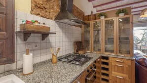 A kitchen with granite countertops, wooden cabinets, a gas stove, and a hanging pot rack.