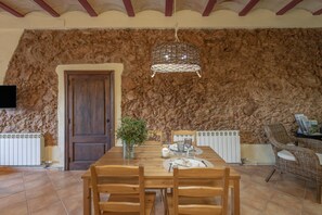 Ein Essbereich mit rustikaler Steinwand, einem Holztisch, Stühlen und einer hängenden Lampe.