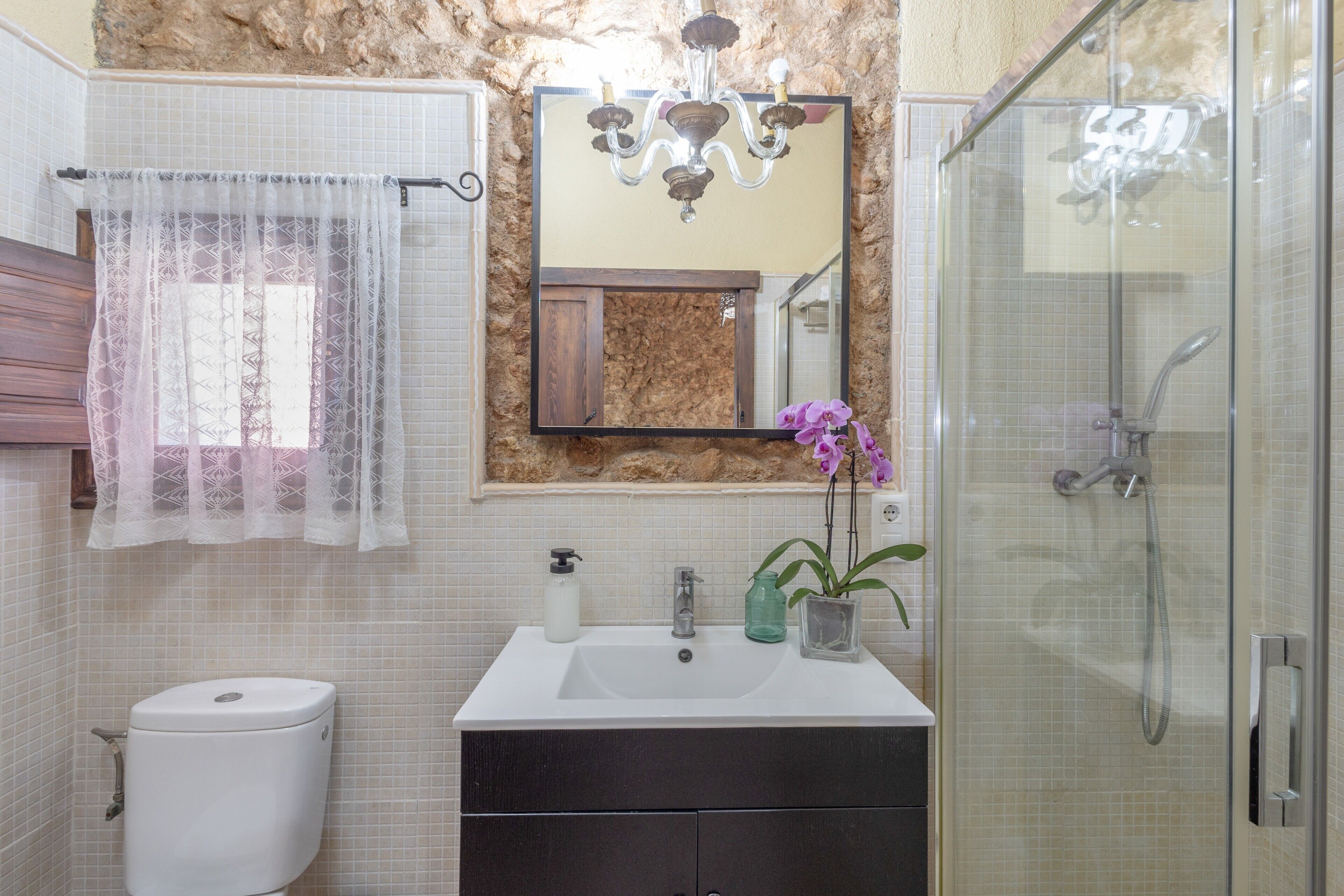 Une salle de bain équipée de toilettes, d’un lavabo, d’une douche et d’un miroir agrémenté d’un lustre.