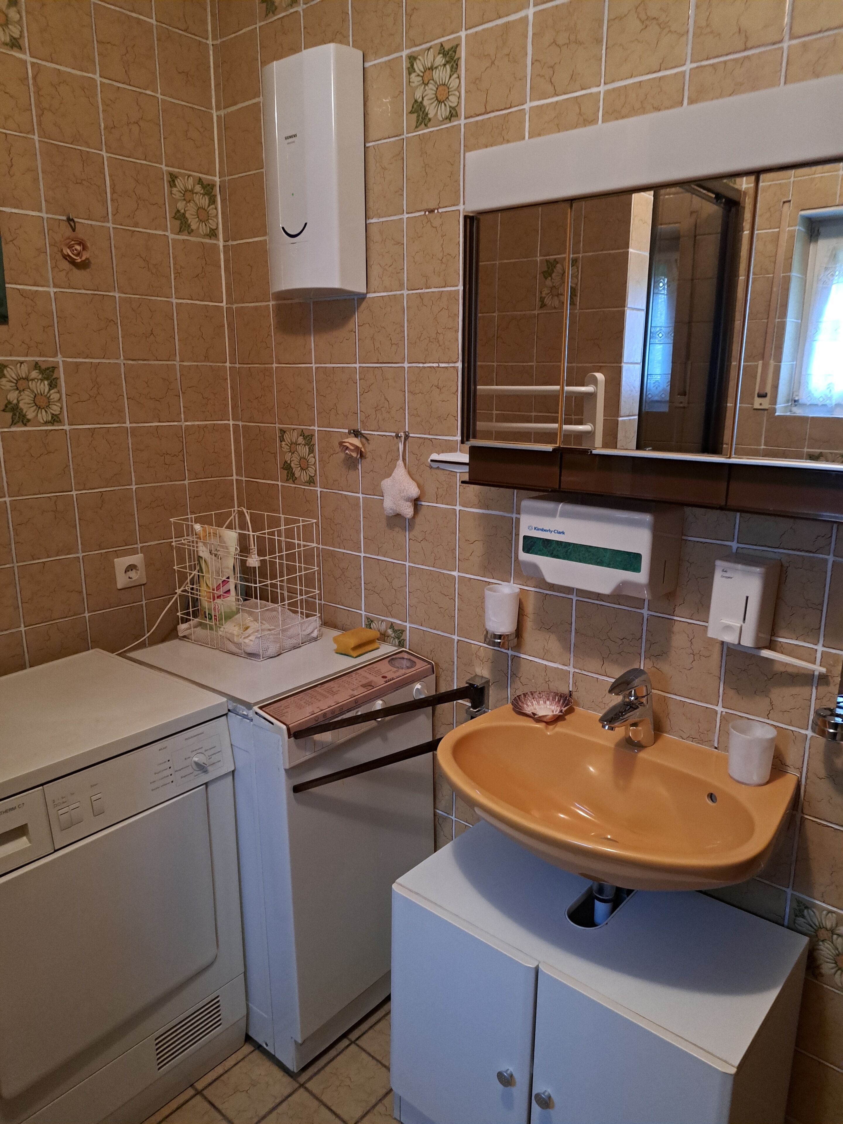 A bathroom with a white sink, a mirror above it, a towel rack, a soap dispenser, and a small cabinet.