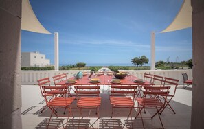 An outdoor dining area with a table set for six, surrounded by red chairs, overlooking a scenic view of the sea and a building. - Exclusive beachfront villa, 6 bedrooms, garden, Monopoli (Monopoli)
