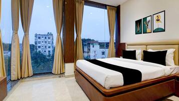 A hotel room with a large bed, a view of buildings through the window, and a wall with framed artwork.