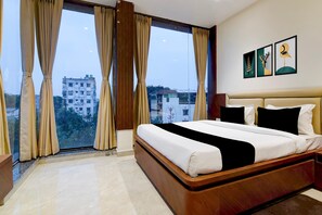 A hotel room with a large bed, a view of buildings through the window, and a wall with framed artwork. - Townhouse OAK Howrah Oak Belilious Park (Howrah)