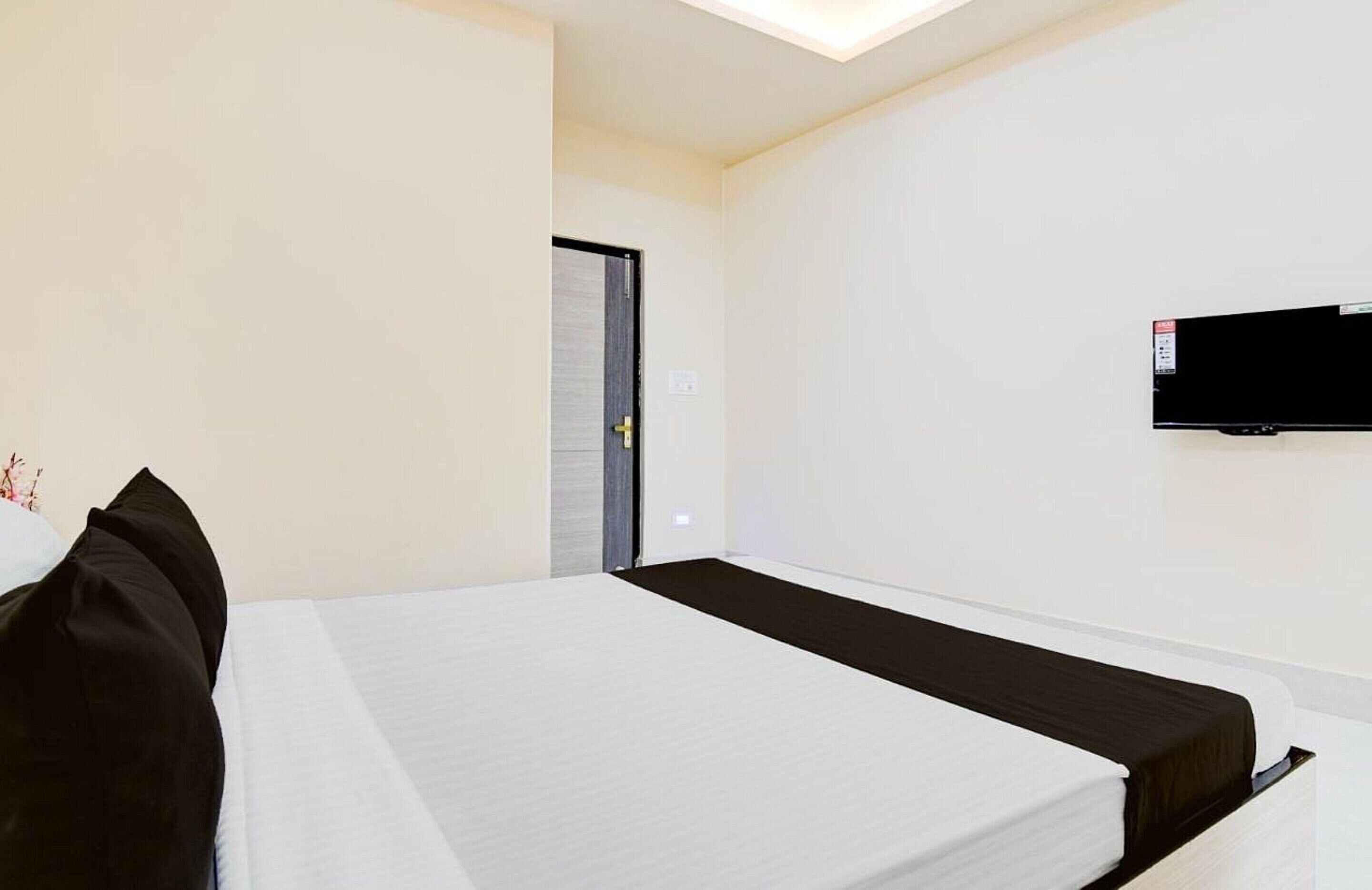 A hotel room with a bed, a television mounted on the wall, and a door leading to another room.