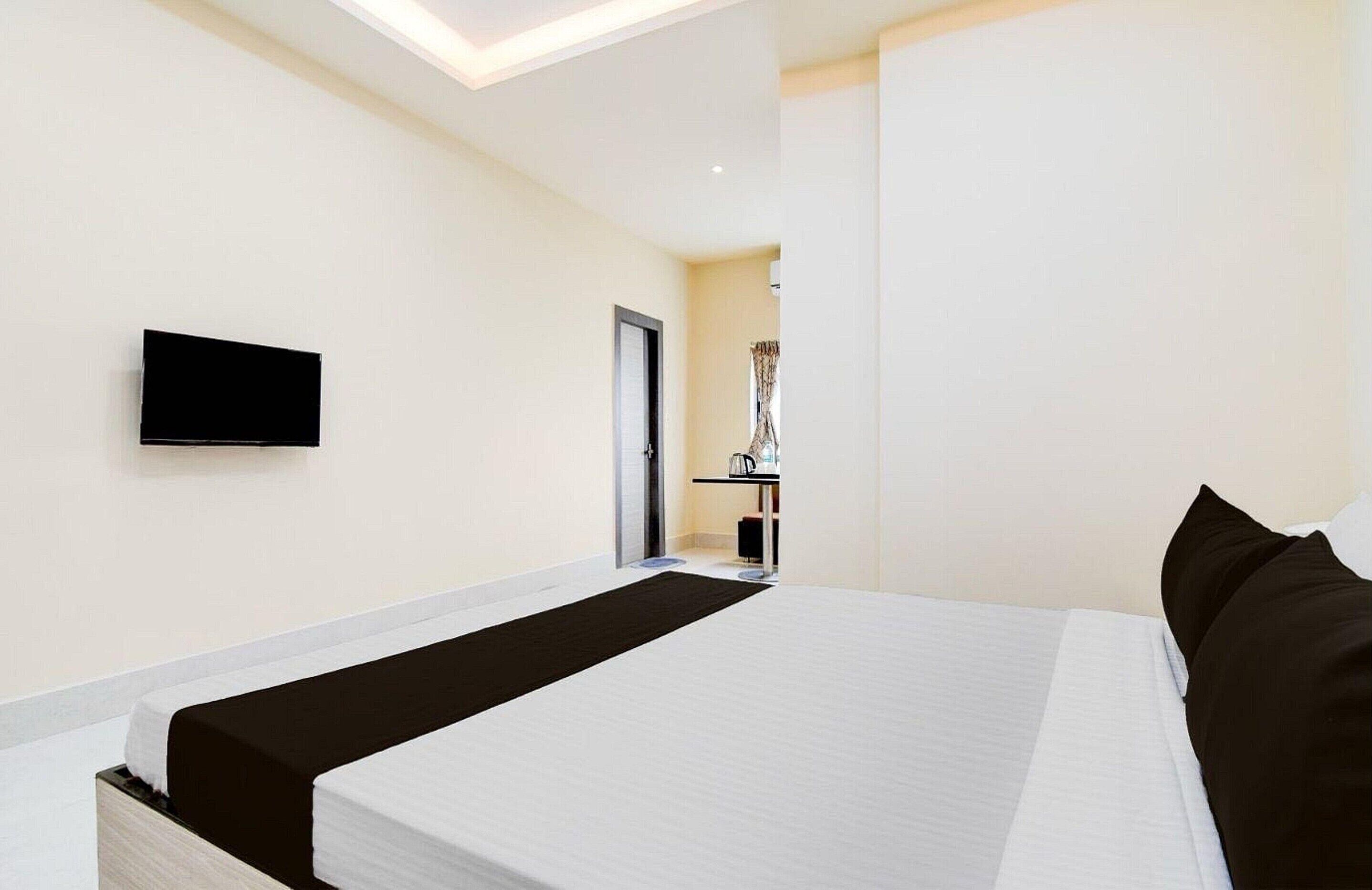 A hotel room with a bed, a flat-screen TV mounted on the wall, and a door leading to a bathroom.