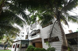 A modern hotel with a white facade, multiple balconies, and a palm tree in the foreground.