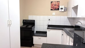 Une cuisine avec des meubles blancs, une cuisinière noire et un dosseret carrelé.