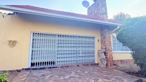 Une maison avec une cheminée en pierre, une porte de garage en métal et un escalier en pierre menant à l’entrée.